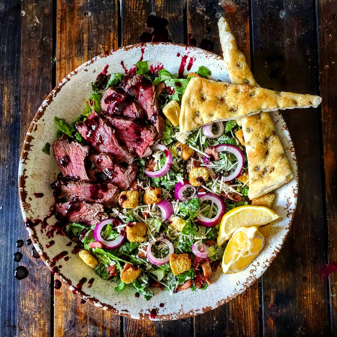 A delicious steak caesar salad with focaccia points.